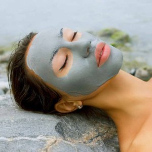 Woman with blue clay facial mask in beauty spa (wellness).